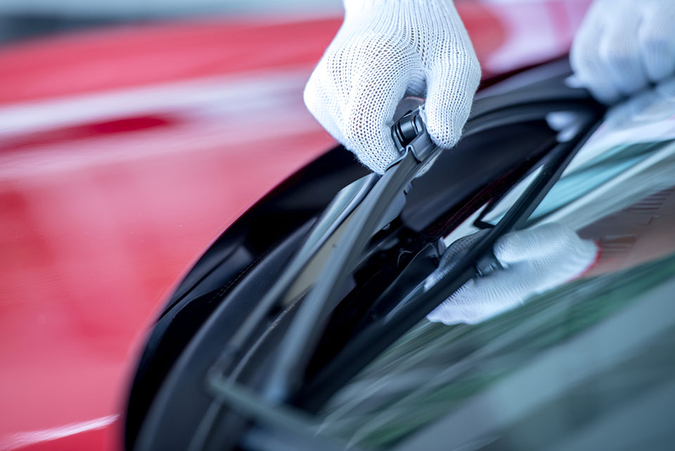 The mechanic is changing the wipers in the parking lot. Change the wiper tires to prepare for the windshield cleaning while raining during the rainy season. Le mécanicien change les essuie-glaces