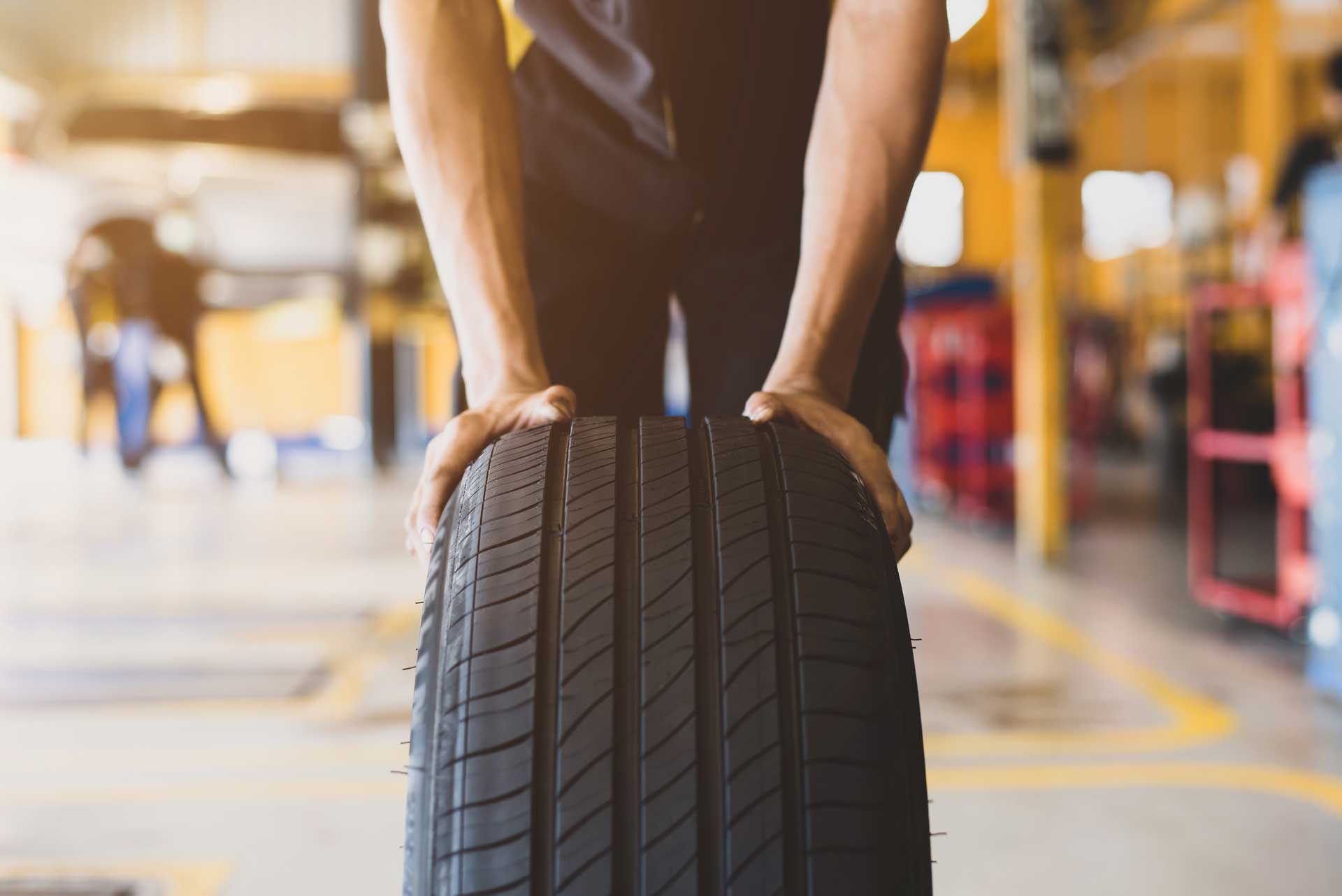 A handsome young mechanic in white gloved uniform is putting his hand on a new tire and checking and checking the condition of the tire while doing car service. Le rôle du pneu